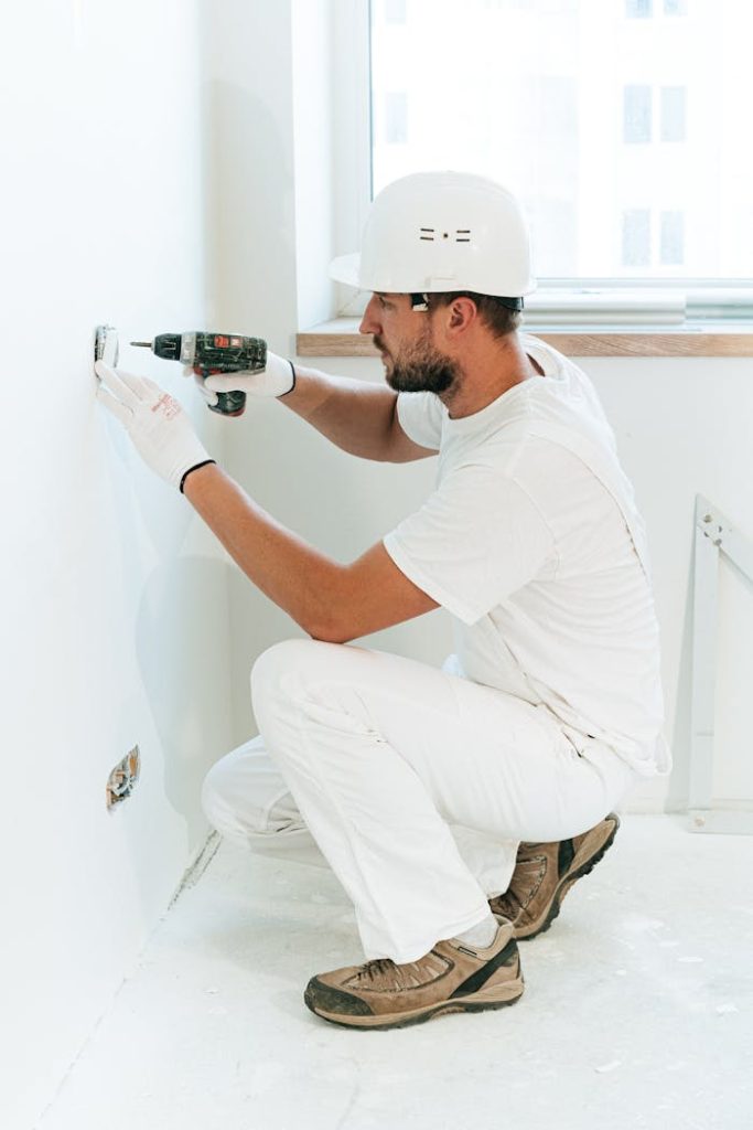 man-drilling-in-a-wall-in-an-apartment-4981802 A construction worker wearing a helmet uses a drill to install a wall outlet inside an apartment.